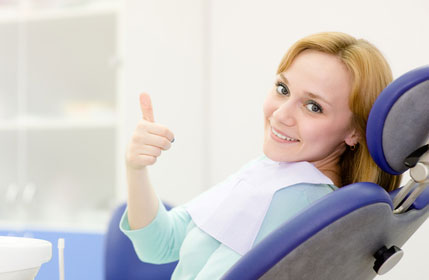 Woman in a dental chair giving a thumbs up.